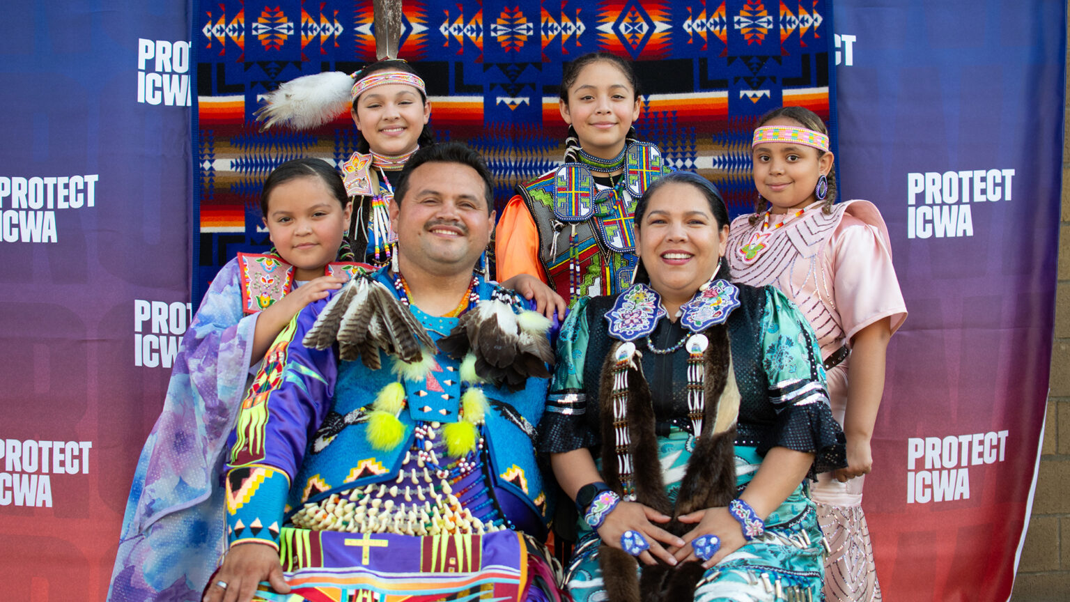 Native family with mother, father, and four children smiling in front of a fabric backdrop.